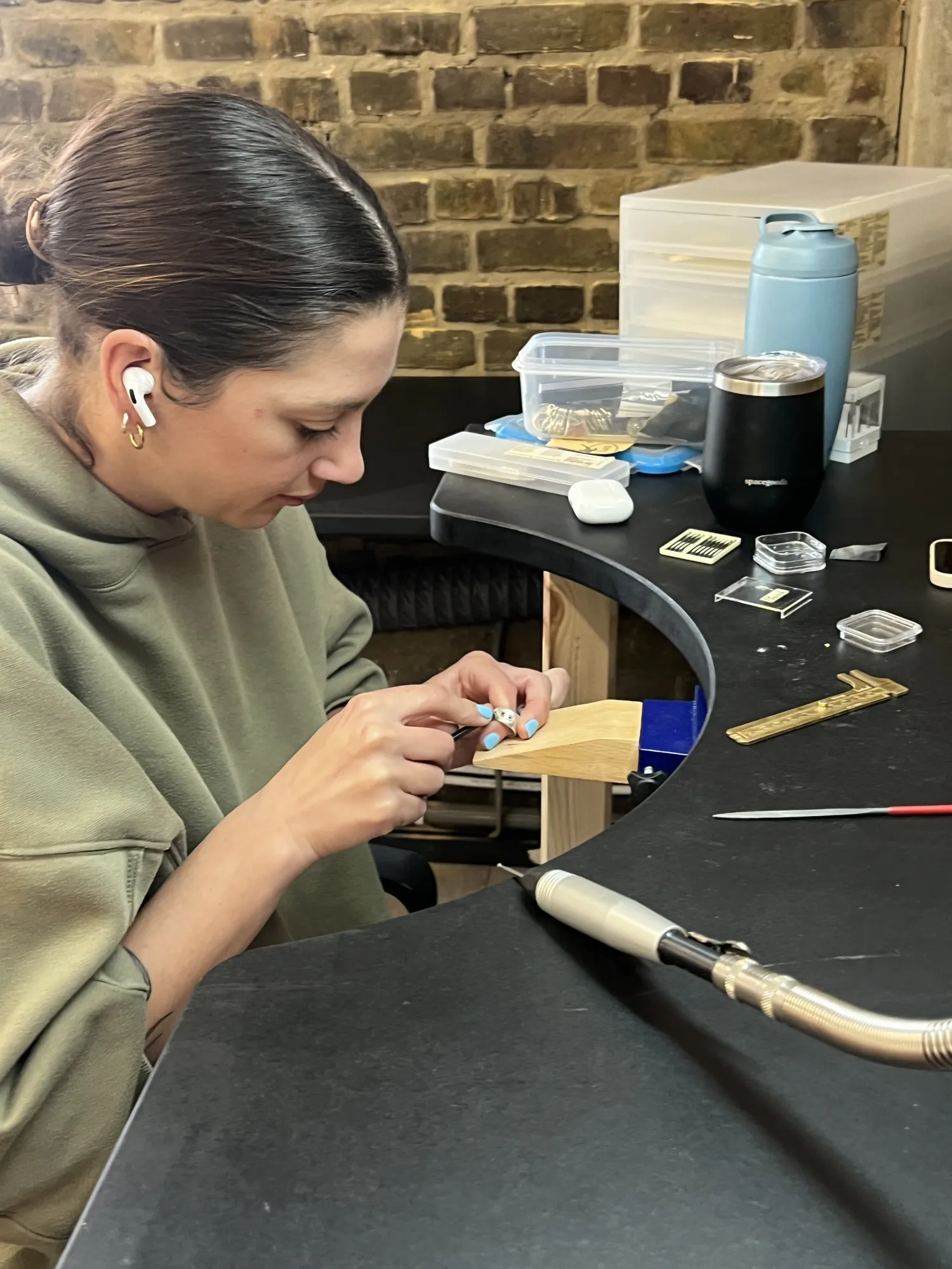 A jeweller filing at her bench against the brick wall